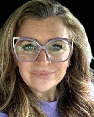Acounselor with light brown hair, wearing large purple glasses and a purple shirt, smiling at the camera.