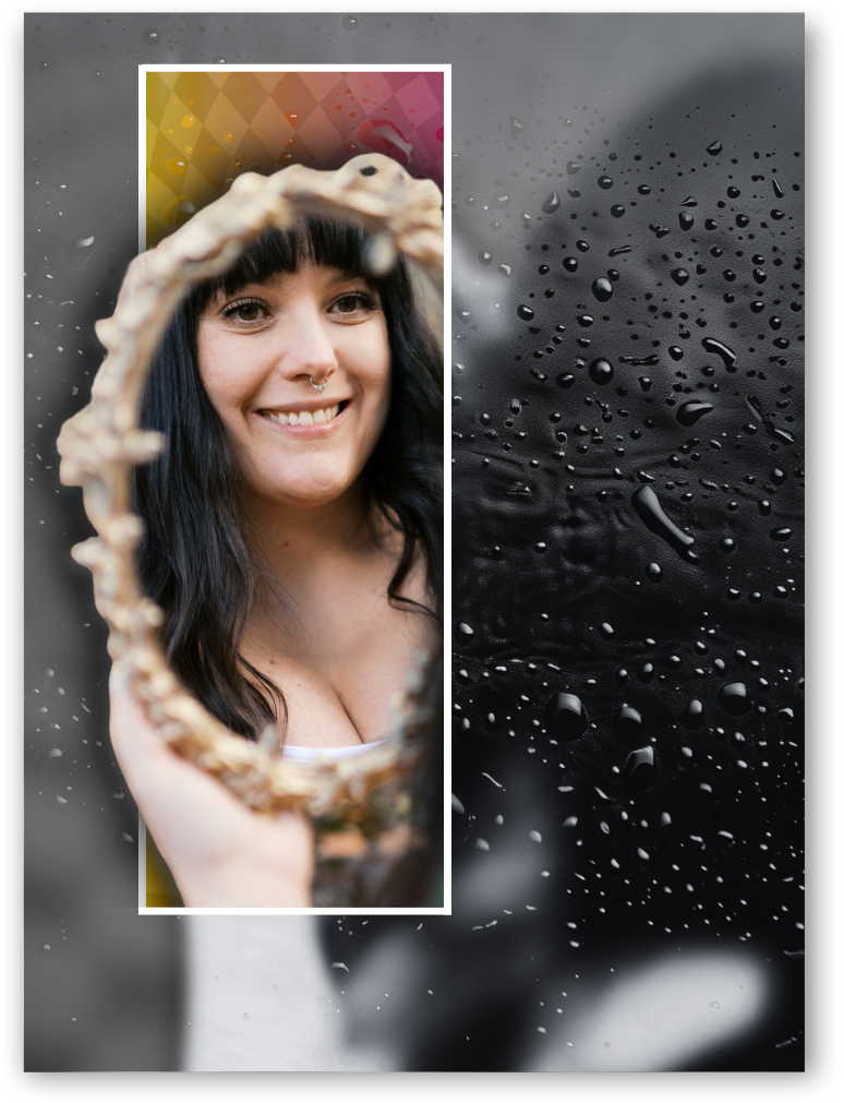A woman with black hair and a nose piercing is smiling while looking at her reflection in a hand mirror.