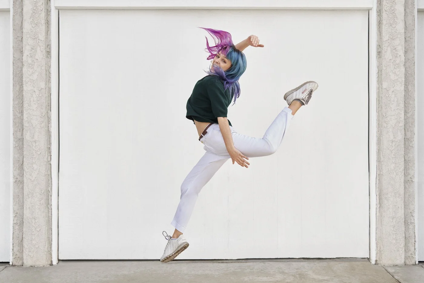 woman with pink and purple hair jumping excitedly in front of wall