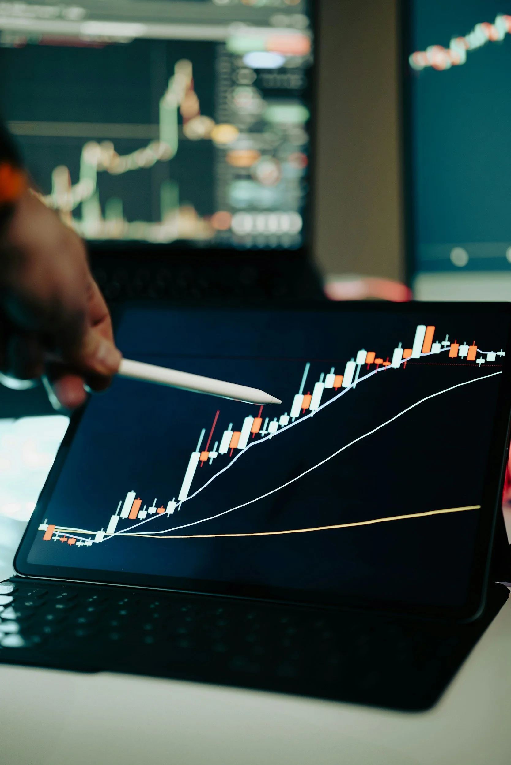 A person is analyzing a stock chart on a computer screen, with two monitors displaying financial data, focusing on a candlestick chart showing stock price movements.