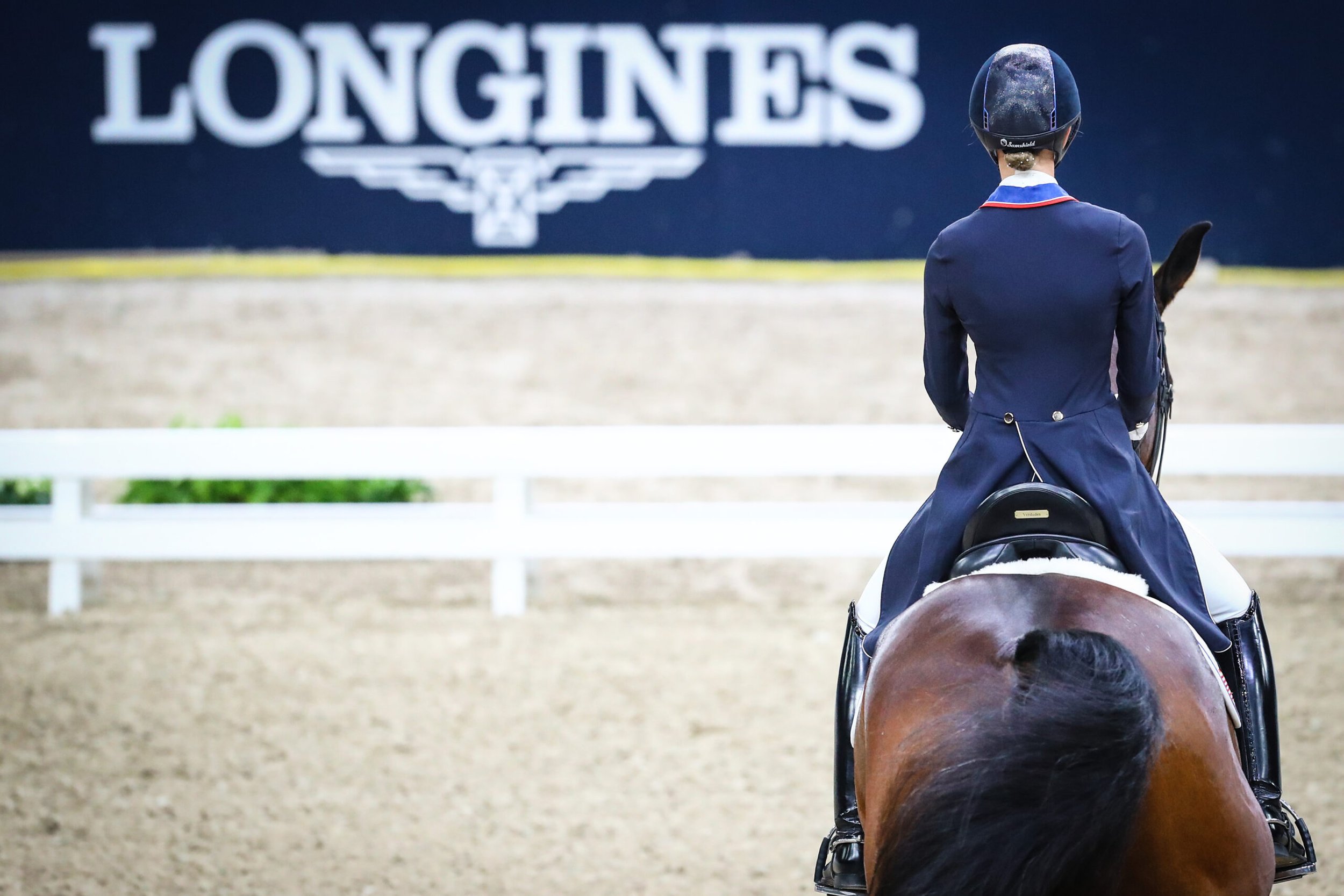 Reiterin in dunkler Turnierkleidung auf einem Pferd vor dem Longines-Schild in einer Reitarena