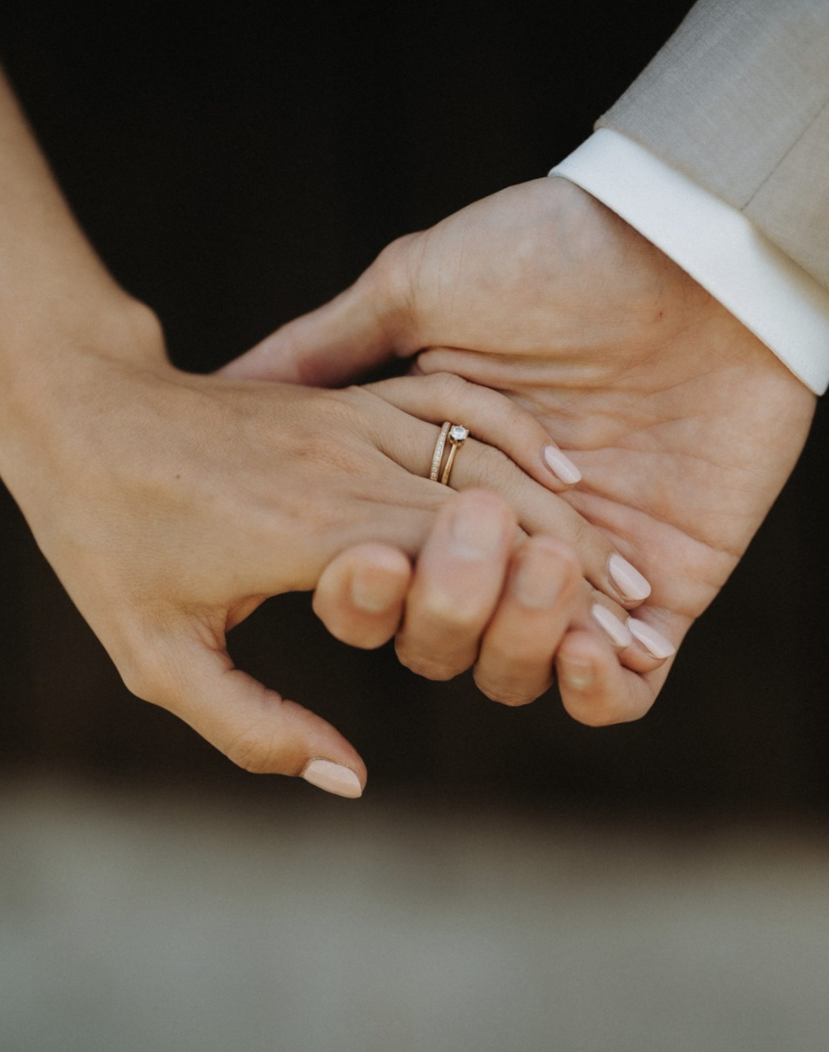Nahaufnahme eines Paares, das sich an den Händen hält; eine Hand trägt einen goldenen Verlobungsring mit Diamant.