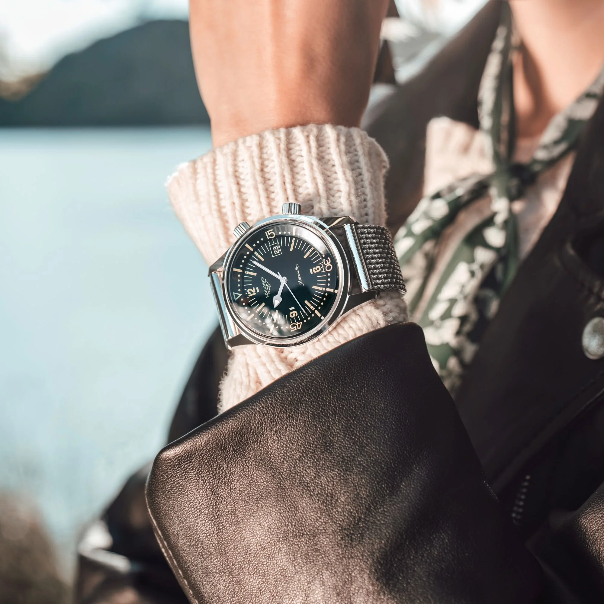 Nahaufnahme einer Longines-Armbanduhr mit schwarzem Zifferblatt und Metallarmband an einem mit Strickpullover bekleideten Handgelenk