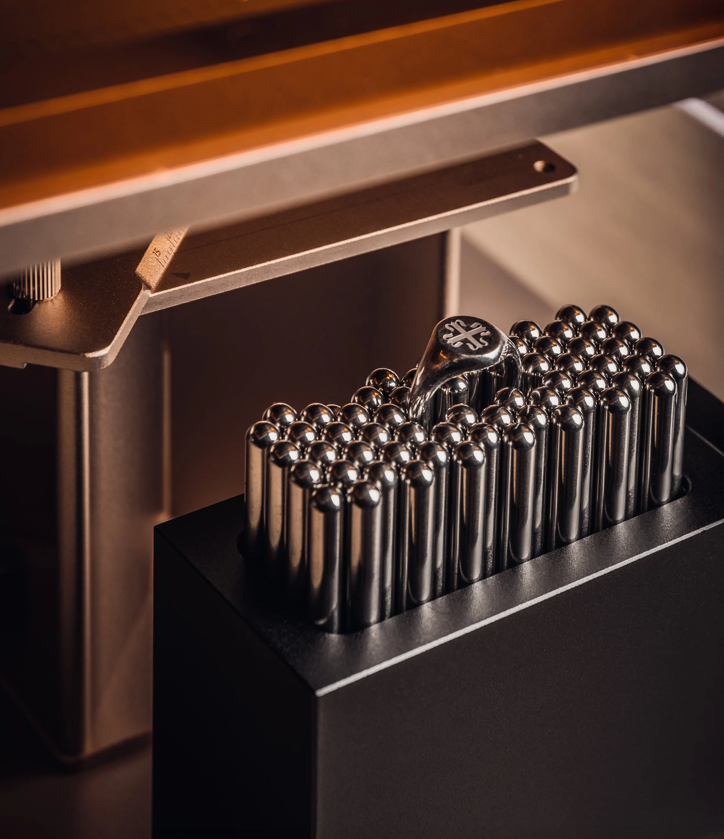 Nahaufnahme eines schwarzen Metalllineals und einer dekorativen Kugelschreiberhalterung mit glänzenden Metallstiften auf einem Schreibtisch.