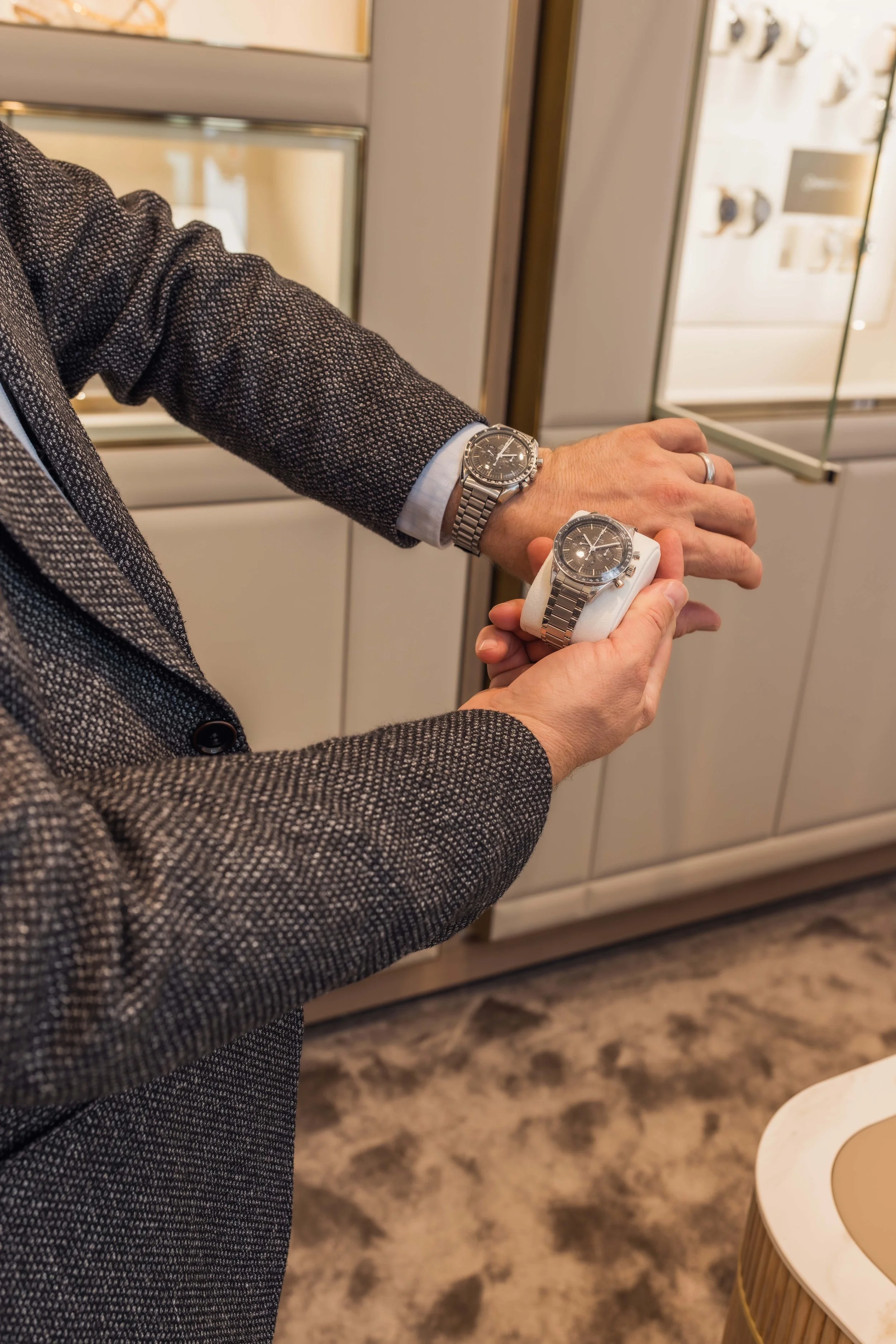 Mann im Anzug vergleicht zwei luxuriöse Chronographen in einer Uhrenboutique.