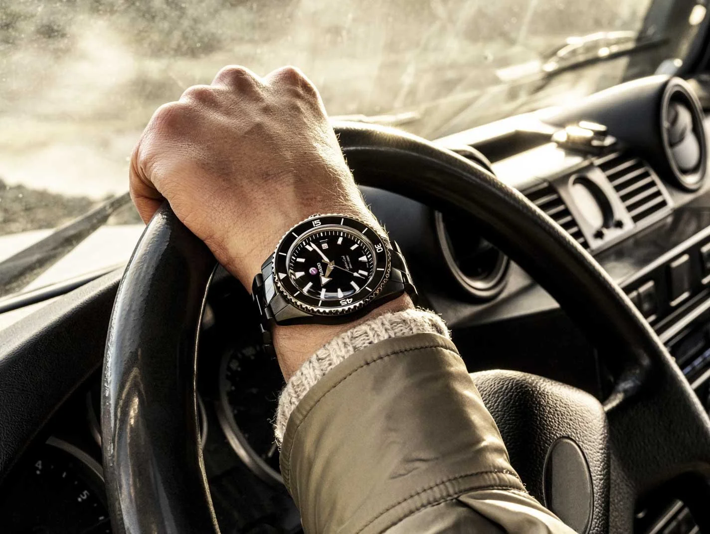 Hand mit schwarzer Taucheruhr am Lenkrad eines Autos