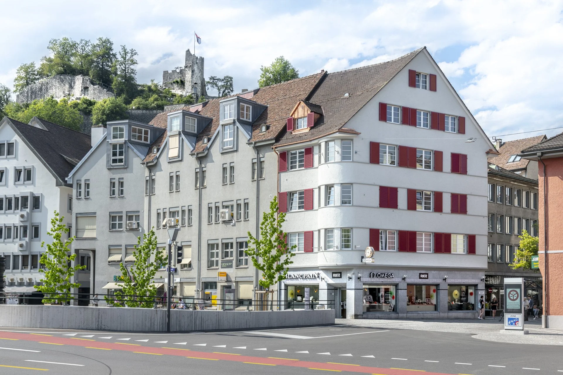 Stadtansicht mit historischen Häusern, Geschäften und mittelalterlicher Burg auf einem Felsen im Hintergrund