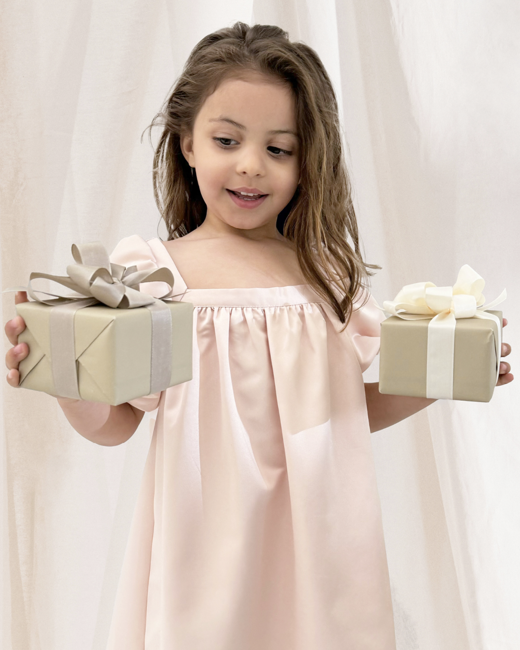 Mädchen im rosa Kleid hält zwei verpackte Geschenke mit Schleifen.