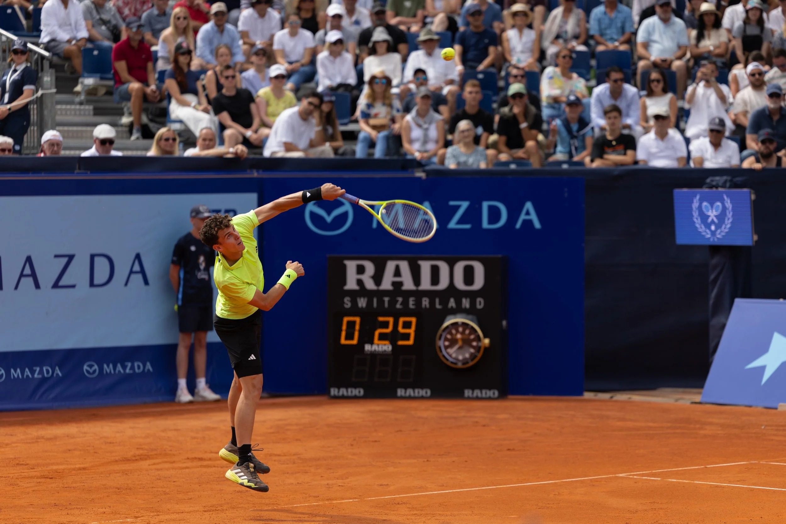 Tennisspieler schlägt auf einem Sandplatz vor Zuschauern den Ball.