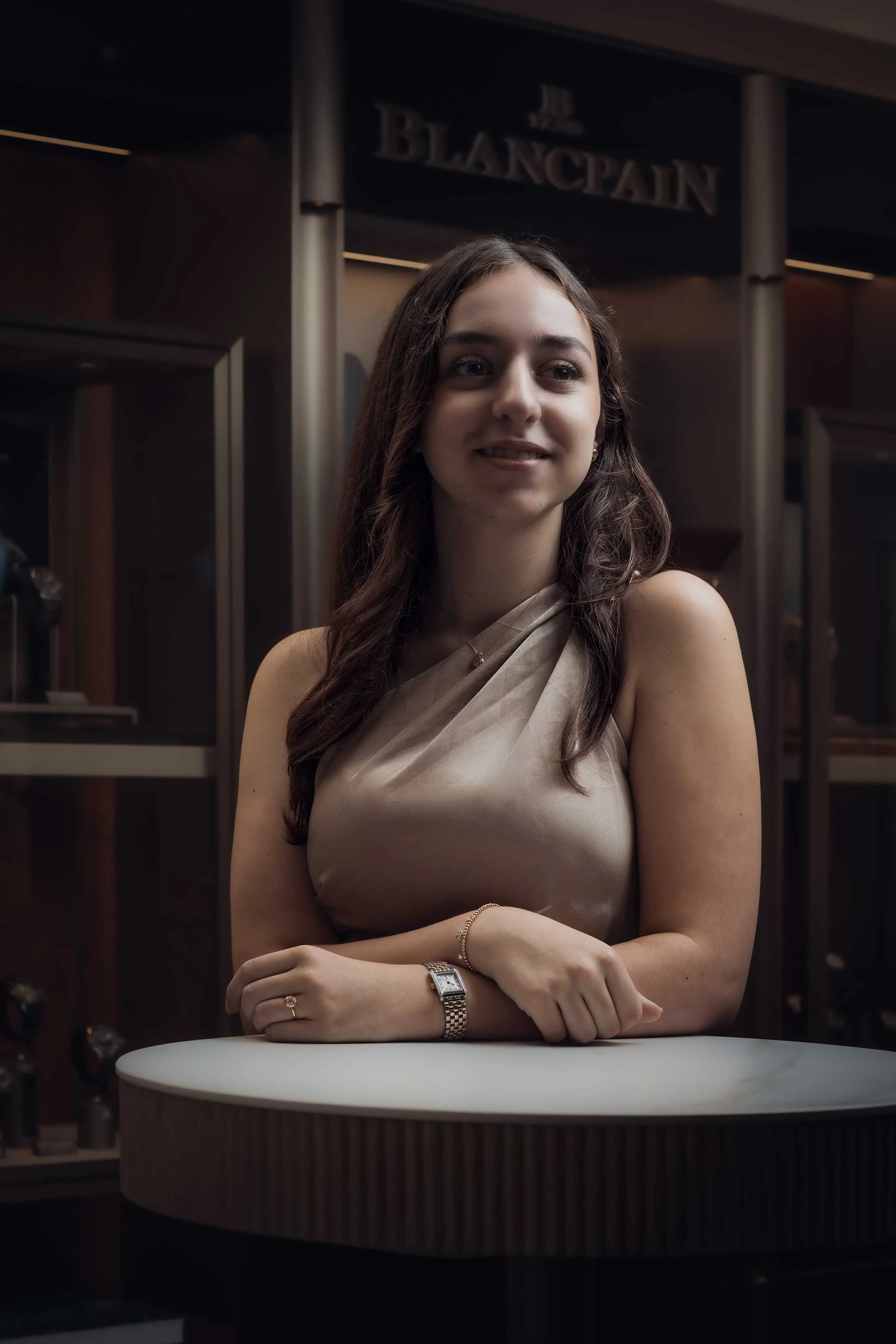 Porträt einer lächelnden jungen Frau mit langen braunen Haaren und Armbanduhr an einem Tisch in einem Restaurant
