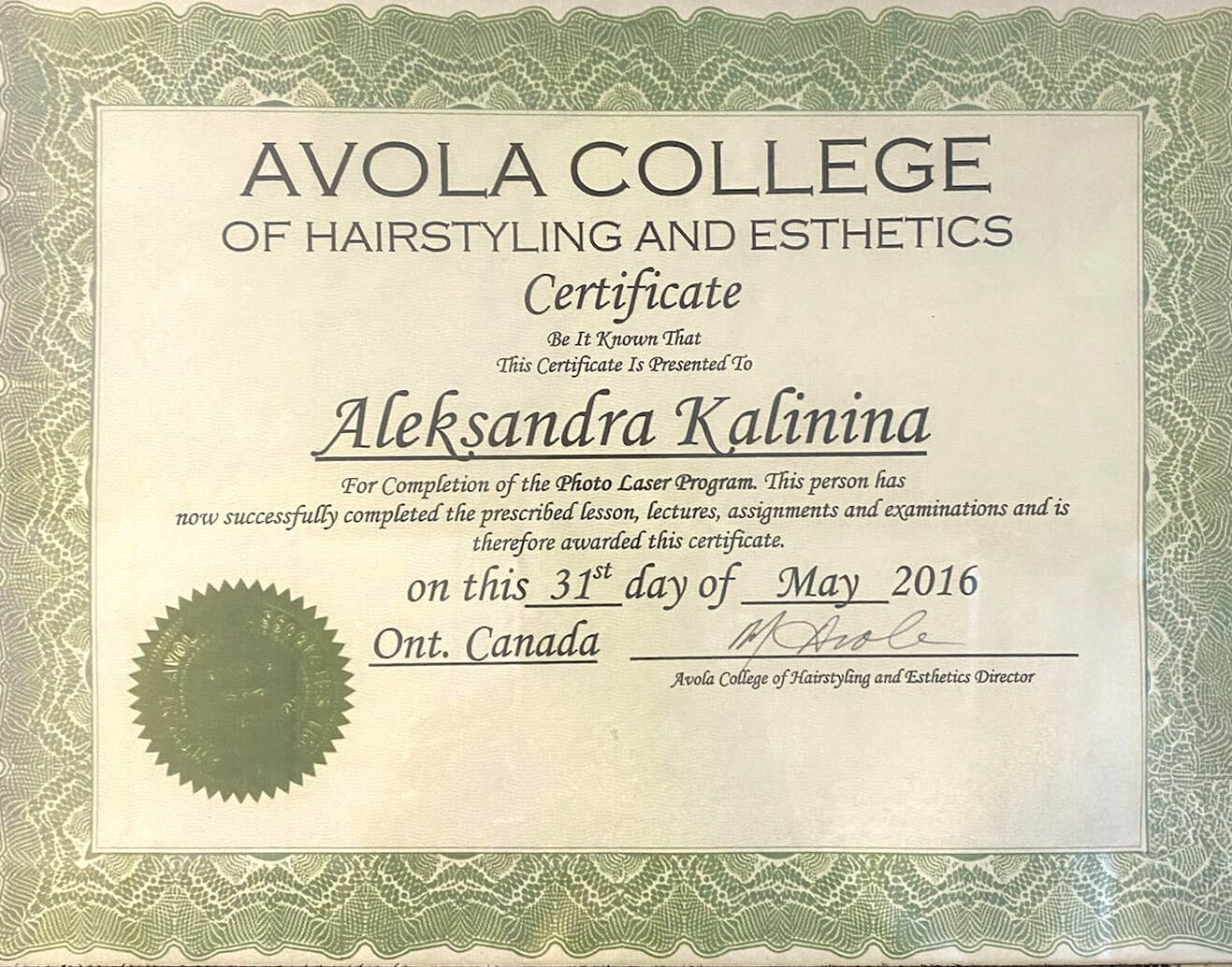 A framed certificate from Avola College of Hairstyling and Esthetics awarded to Aleksandra Kalinina on May 31, 2016, in Ontario, Canada, with decorative green border and gold seal.