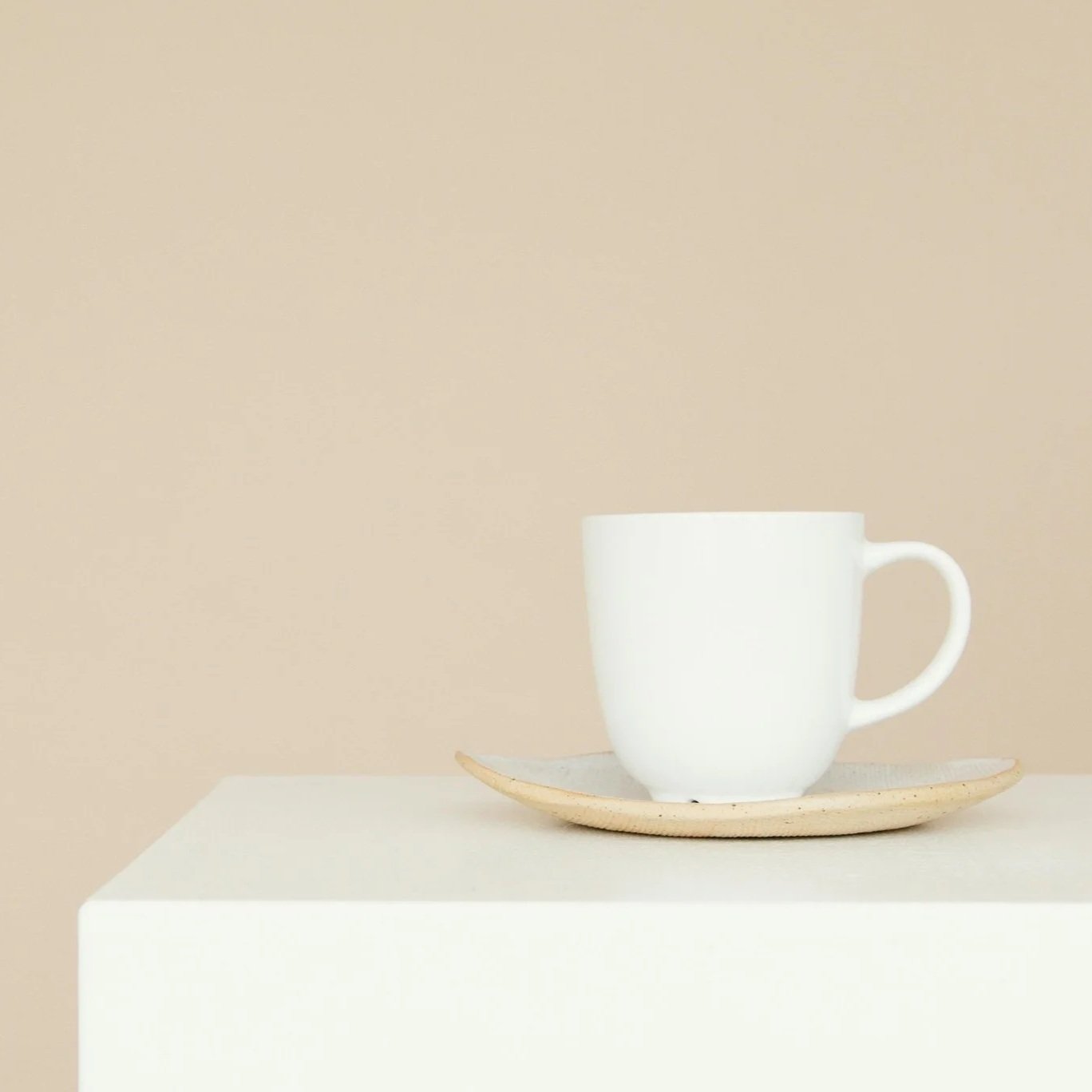 White ceramic mug on a beige plate, placed on a white surface against a beige background.