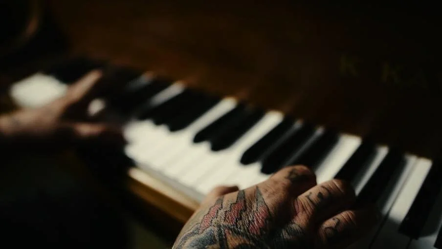 Close-up of tattooed hand playing a piano keyboard.