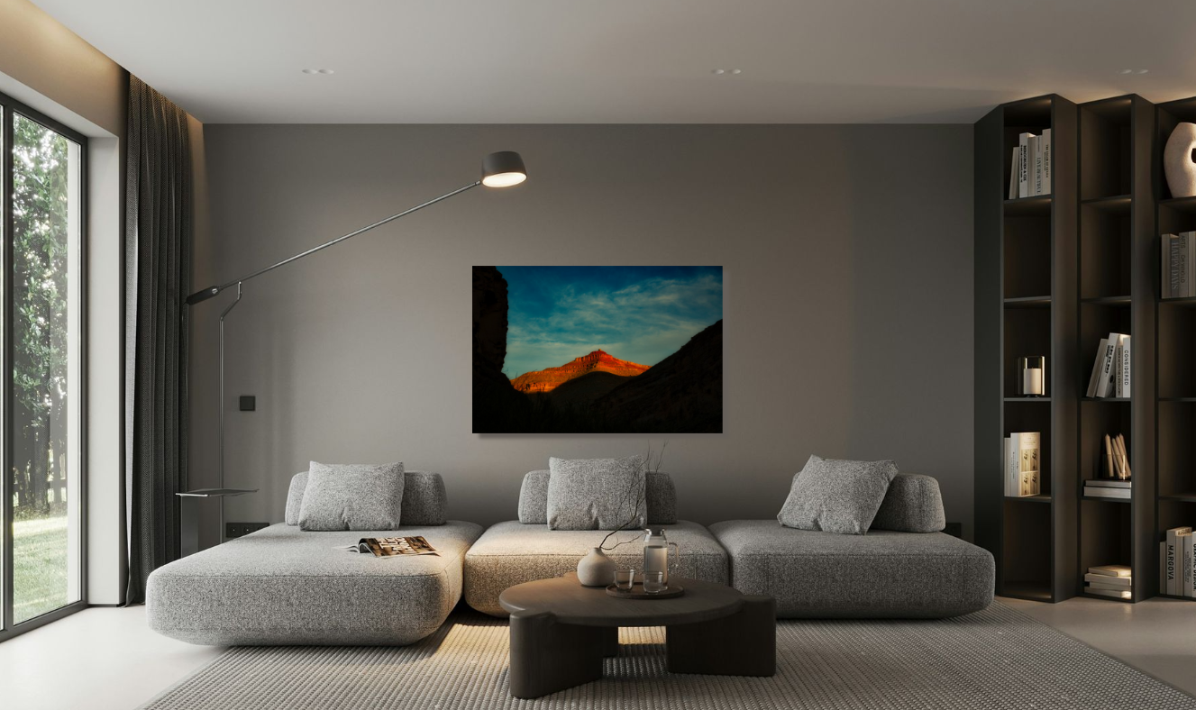 Modern living room with gray sectional sofa, a black floor lamp, and a bookshelf, with a outdoor landscape photo on the gray wall, and sliding glass door with dark curtains.