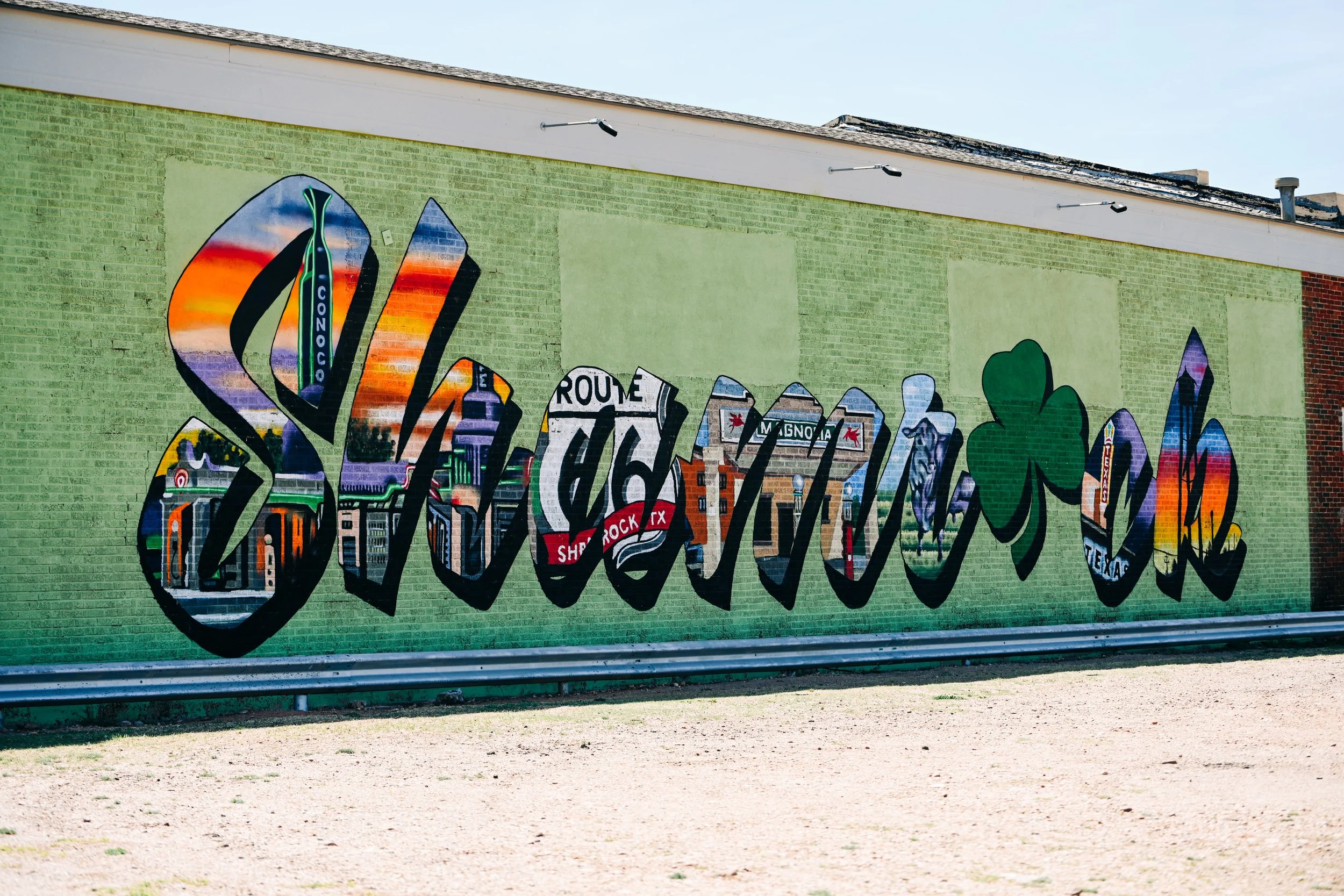 Colorful mural painted on a brick wall with various shapes, including green, purple, and orange, depicting cityscape elements and abstract patterns.