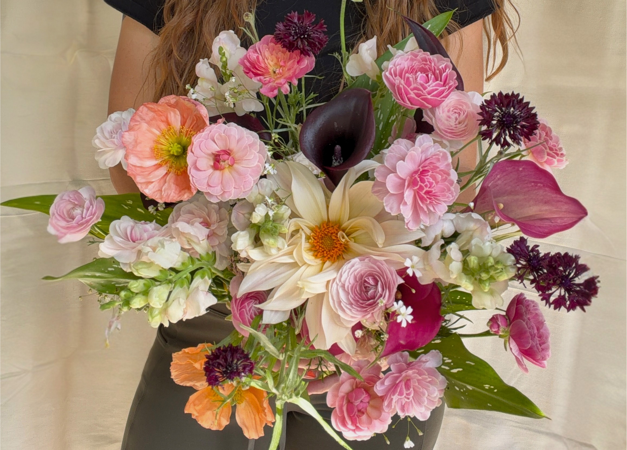 A woman in black clothing holding a large colorful bouquet of various pink, white, orange, and dark purple flowers with green leaves.