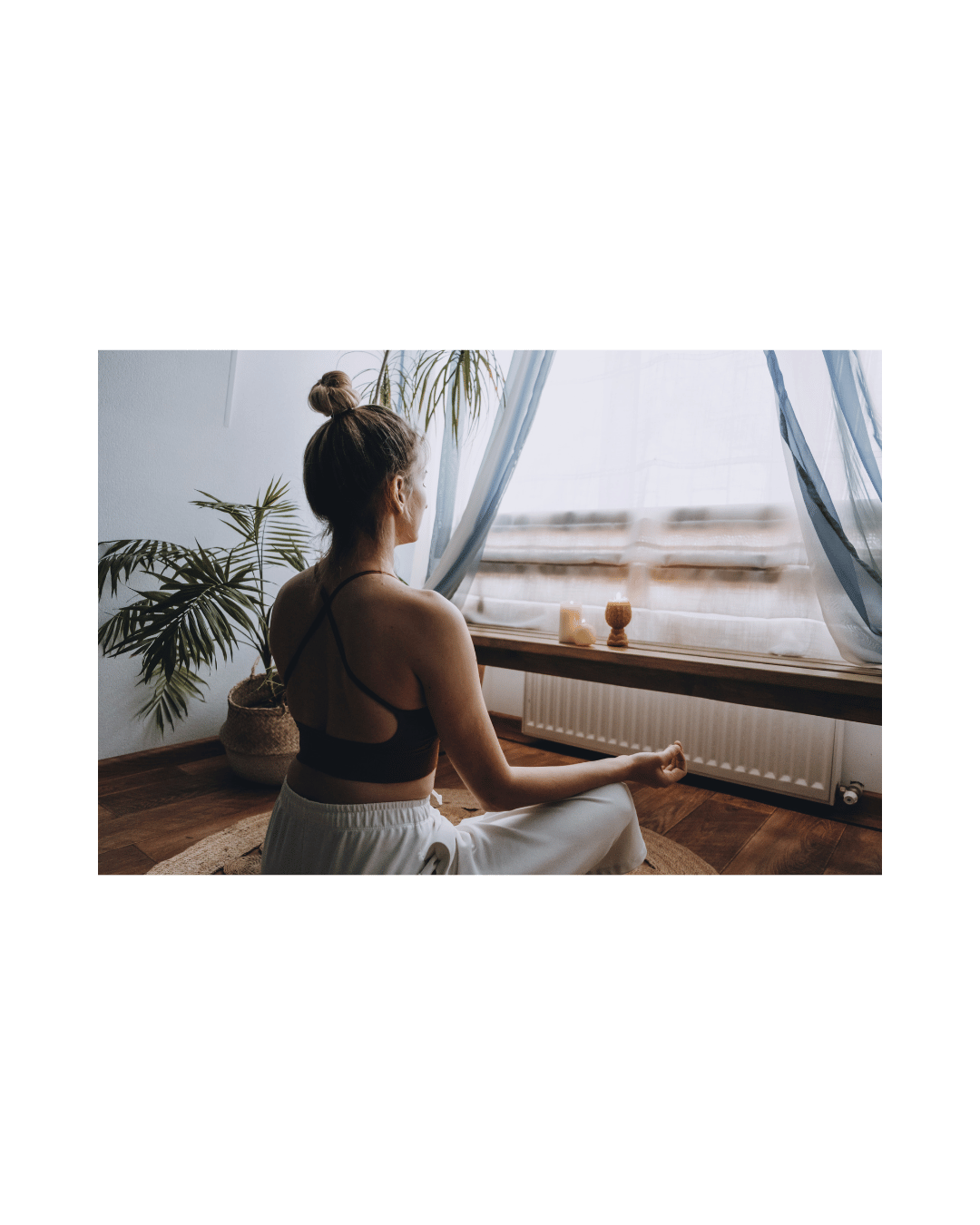 Woman practicing yoga in a sunlit room with potted plants and candles.