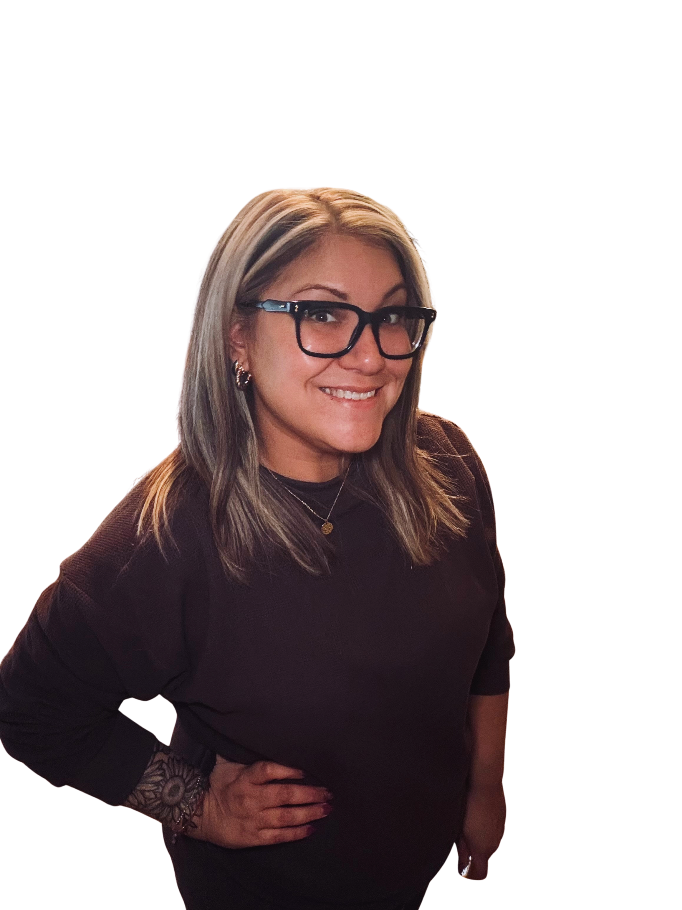 A woman with blonde hair, wearing glasses, earrings, and a dark top, smiling at the camera. She is standing against a black background.