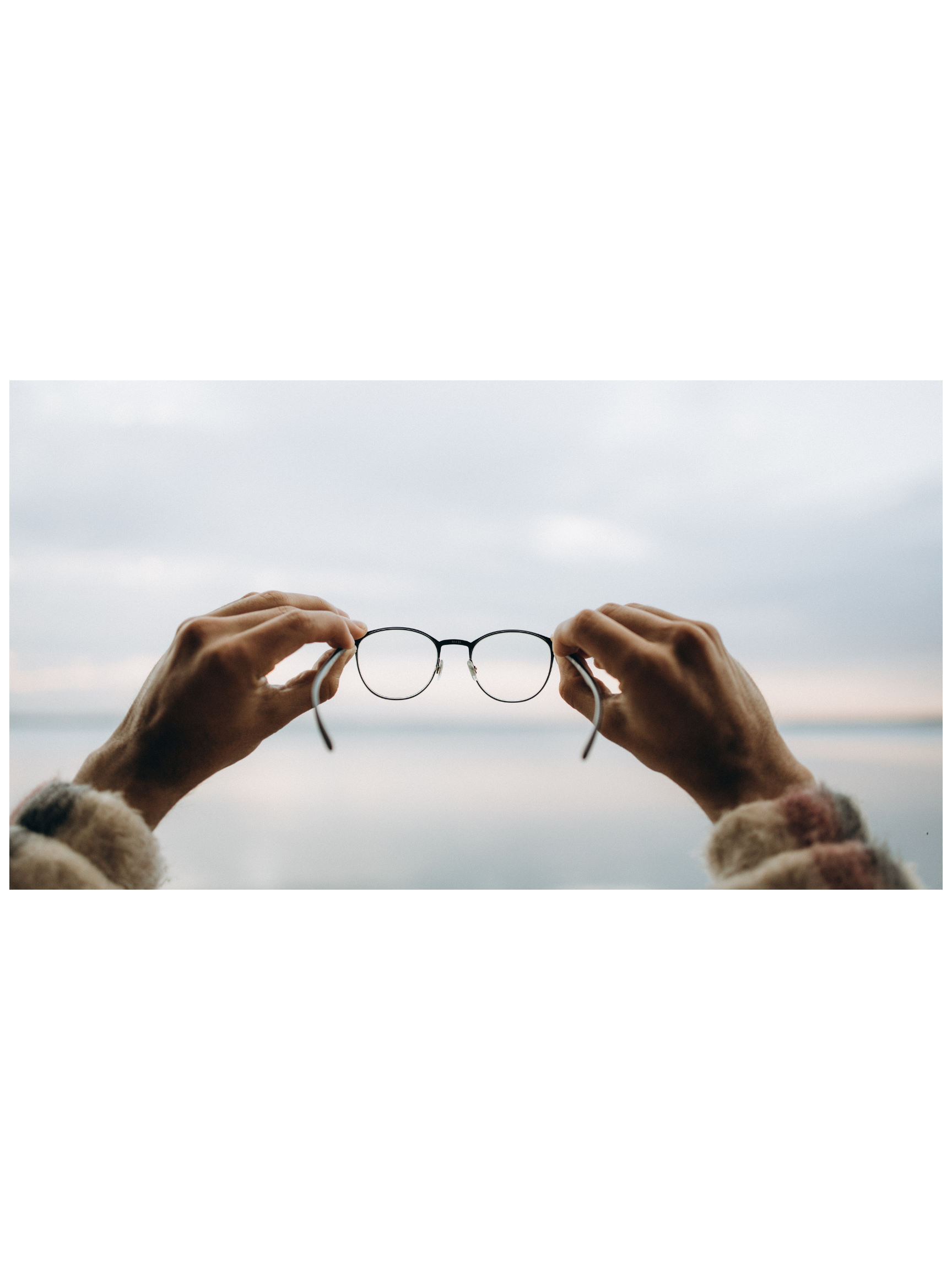 Person holding glasses up against a cloudy sky and ocean background