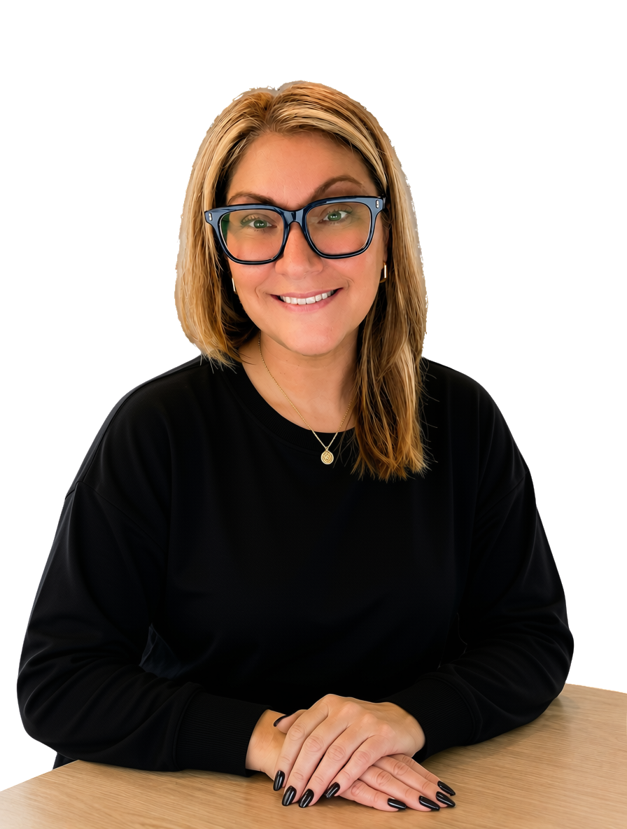 A woman with blonde hair, glasses, and a black top sitting at a wooden table, smiling at the camera.