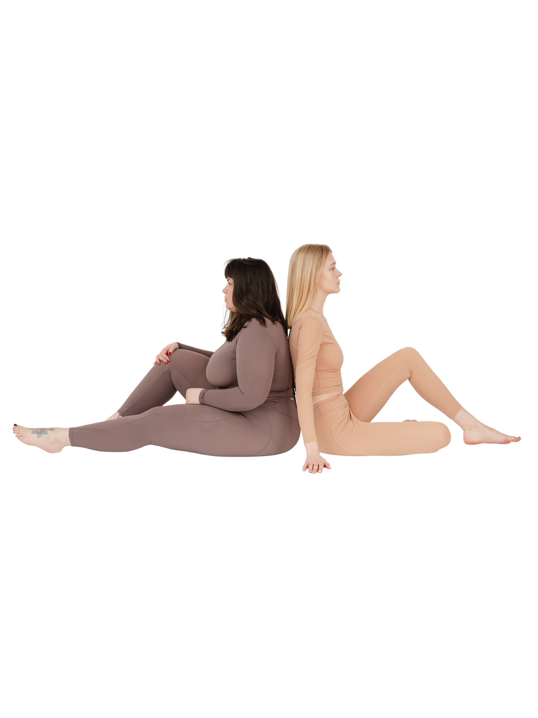Two women sitting back-to-back on the floor with their legs extended and heads resting on their knees, against a black background.