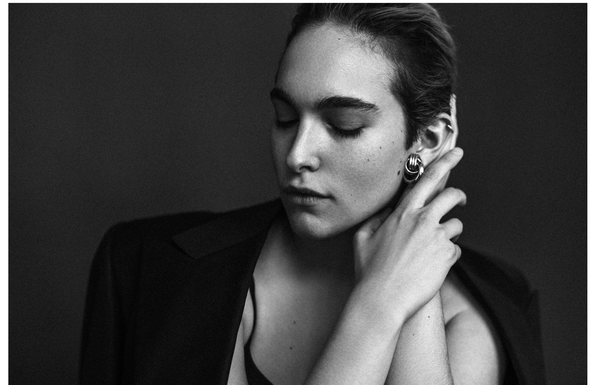 Black and white portrait of a woman with short hair, closed eyes, and earrings, holding her hand near her face