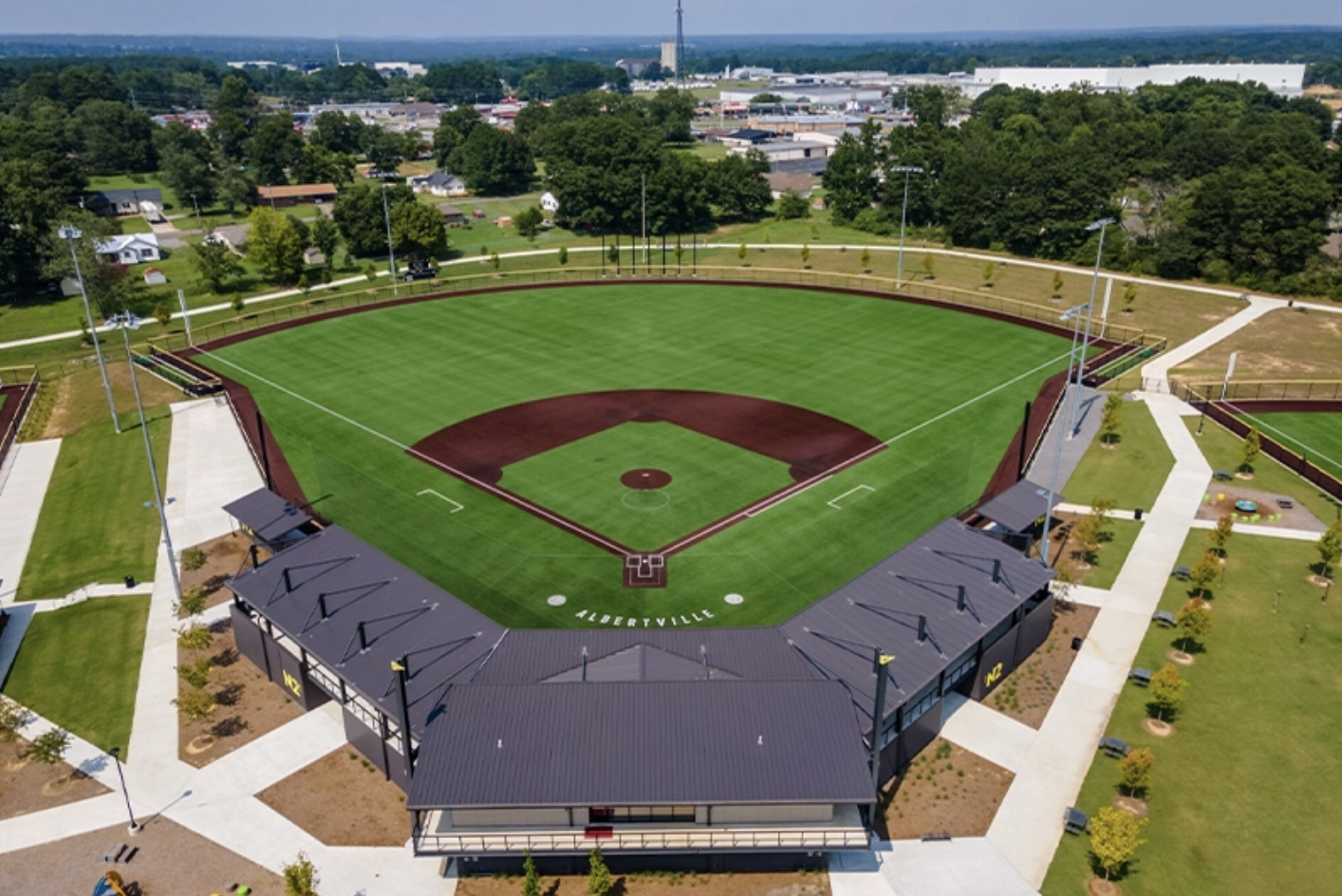 Aerial view of a baseball stadium with green field, brown dirt infield, and surrounding facilities and residential area.