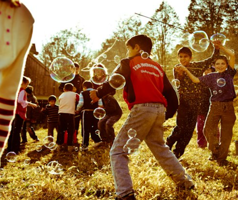 Children playing together among soap bubbles outdoors.