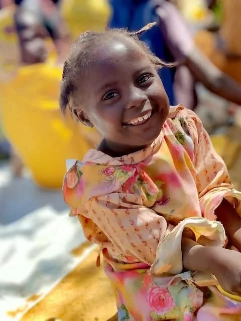 A smiling child in a colourful floral dress, photographed for Bubbles Not Bombs.