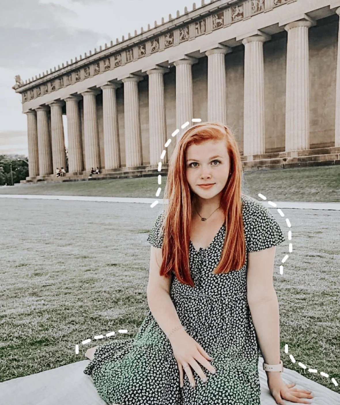 A young woman with red hair sitting on a blanket in front of the Lincoln Memorial at sunset.