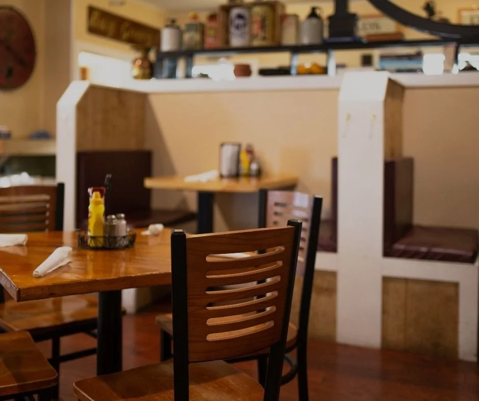 Empty wooden tables and chairs in Swingbelly's restaurant with booth seating and decorative shelves in the background.