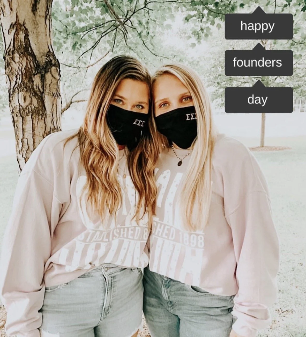 Two women wearing black face masks with Greek letters, standing outdoors under a tree, celebrating Founders Day with a message that says 'happy founders day'.