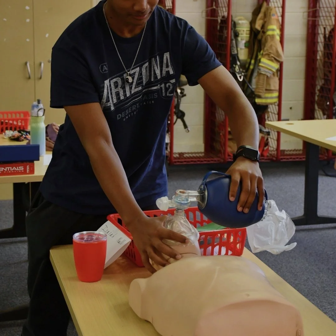 Person practicing CPR on mannequin in a classroom or training room.