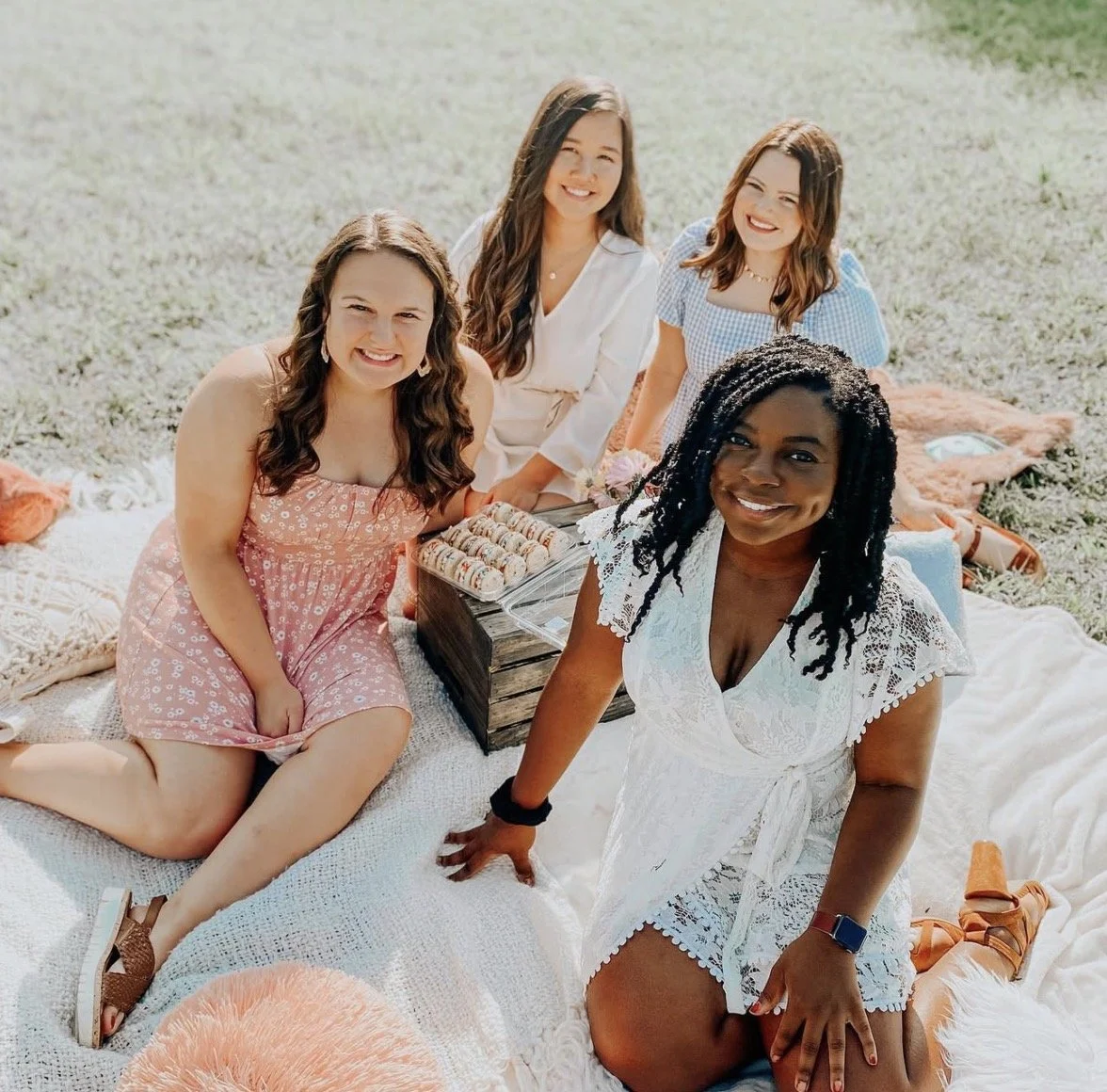 Group of five women having a picnic on a blanket outdoors, smiling at the camera.