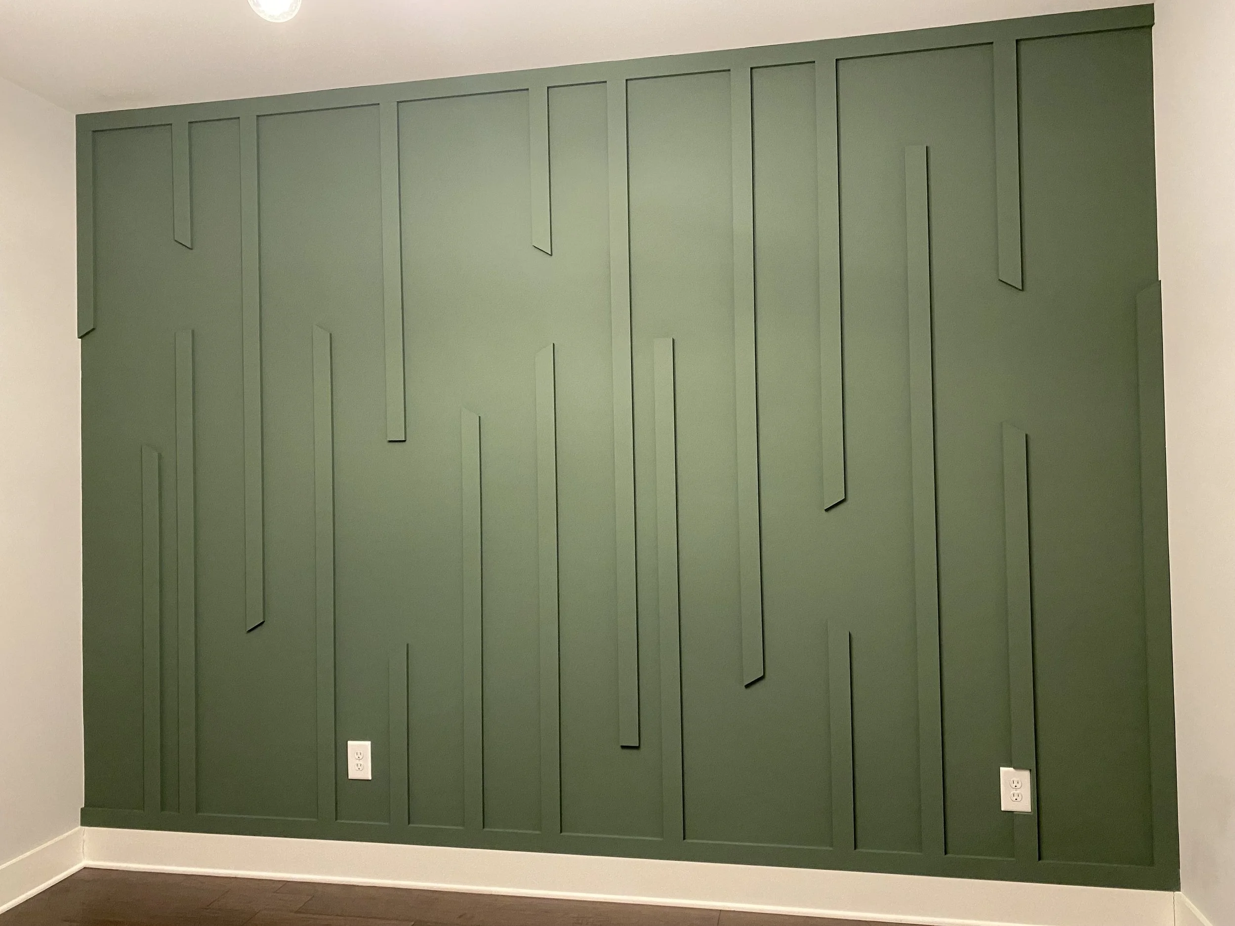 Green feature wall with vertical panels in a room, white electrical outlets near the bottom, and a ceiling light.