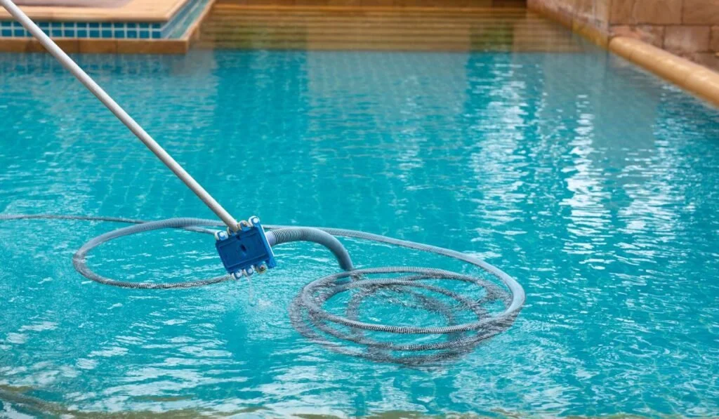 An automatic pool cleaner with a robotic design is submerged in a swimming pool, cleaning the water.