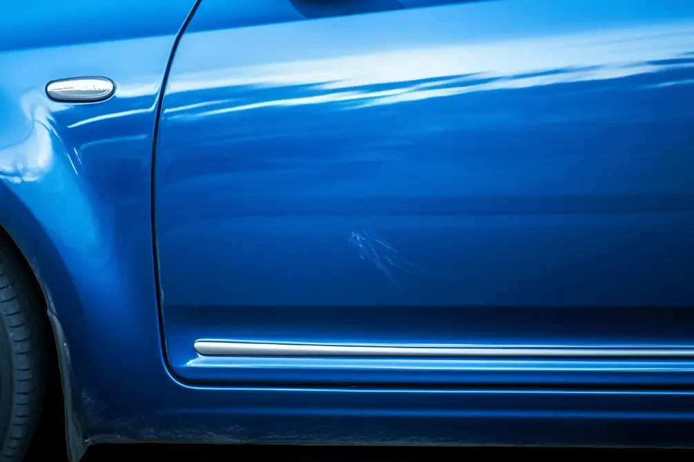 Close-up of a blue car's side showing a scratch on the door