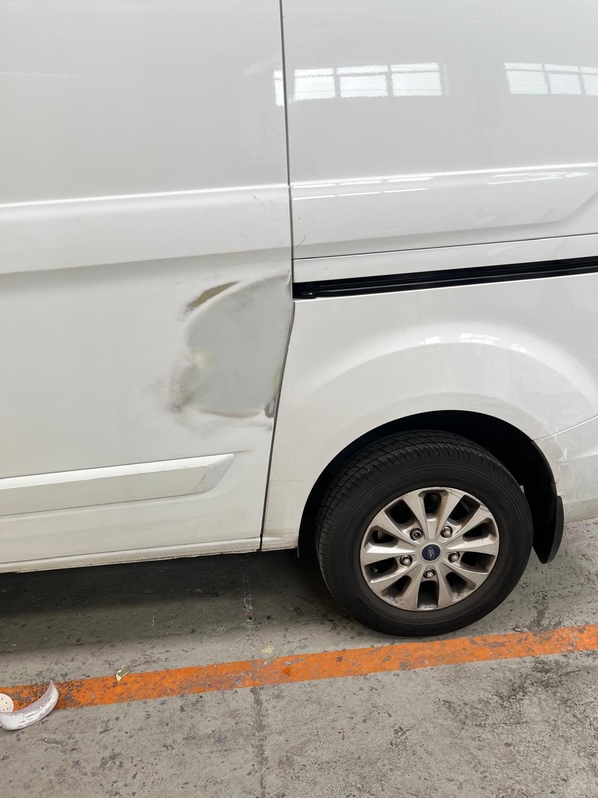 White car with a dent on the driver's side door, parked in a garage with orange parking lines.