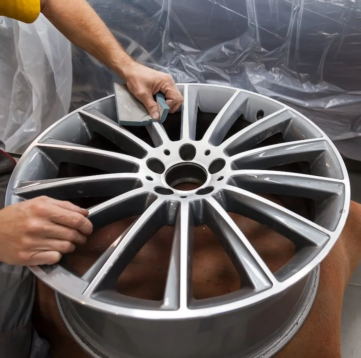 Person polishing or inspecting a silver alloy car wheel rim in a workshop.
