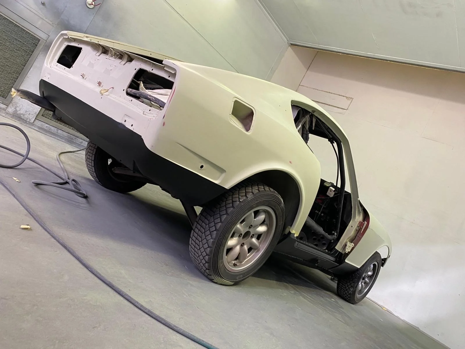 Partially assembled vintage car body without doors or windows, sitting on a concrete floor in a workshop or garage.
