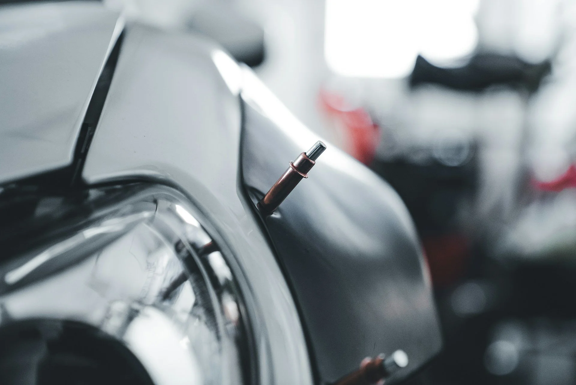 Close-up of the front part of a vintage motorcycle, focusing on the headlight and a small metallic component protruding from the body.