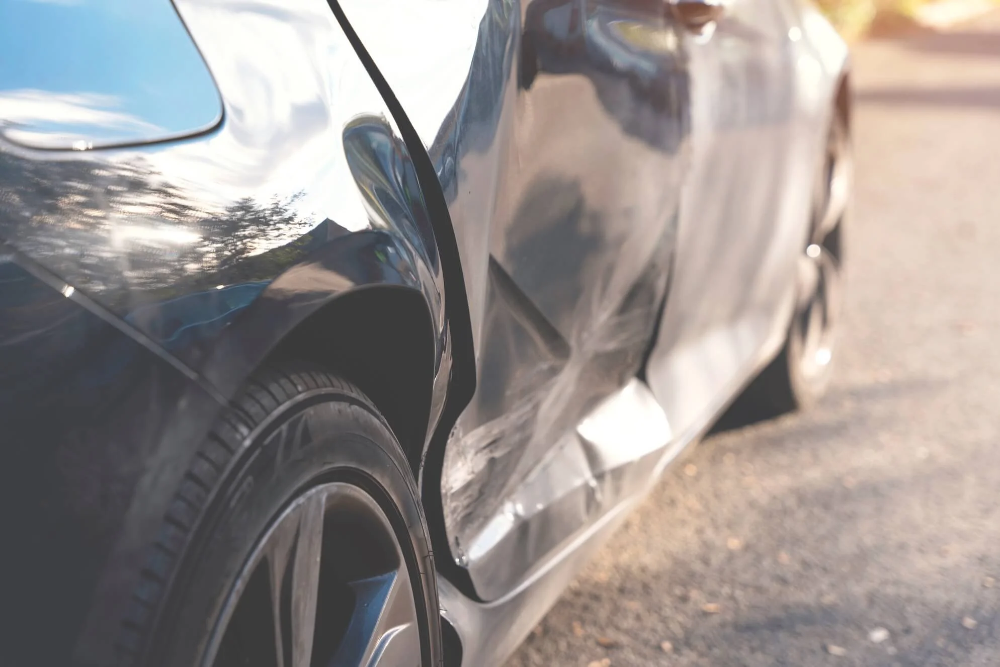 Close-up of a black car with visible damage on the side door and rear panel.