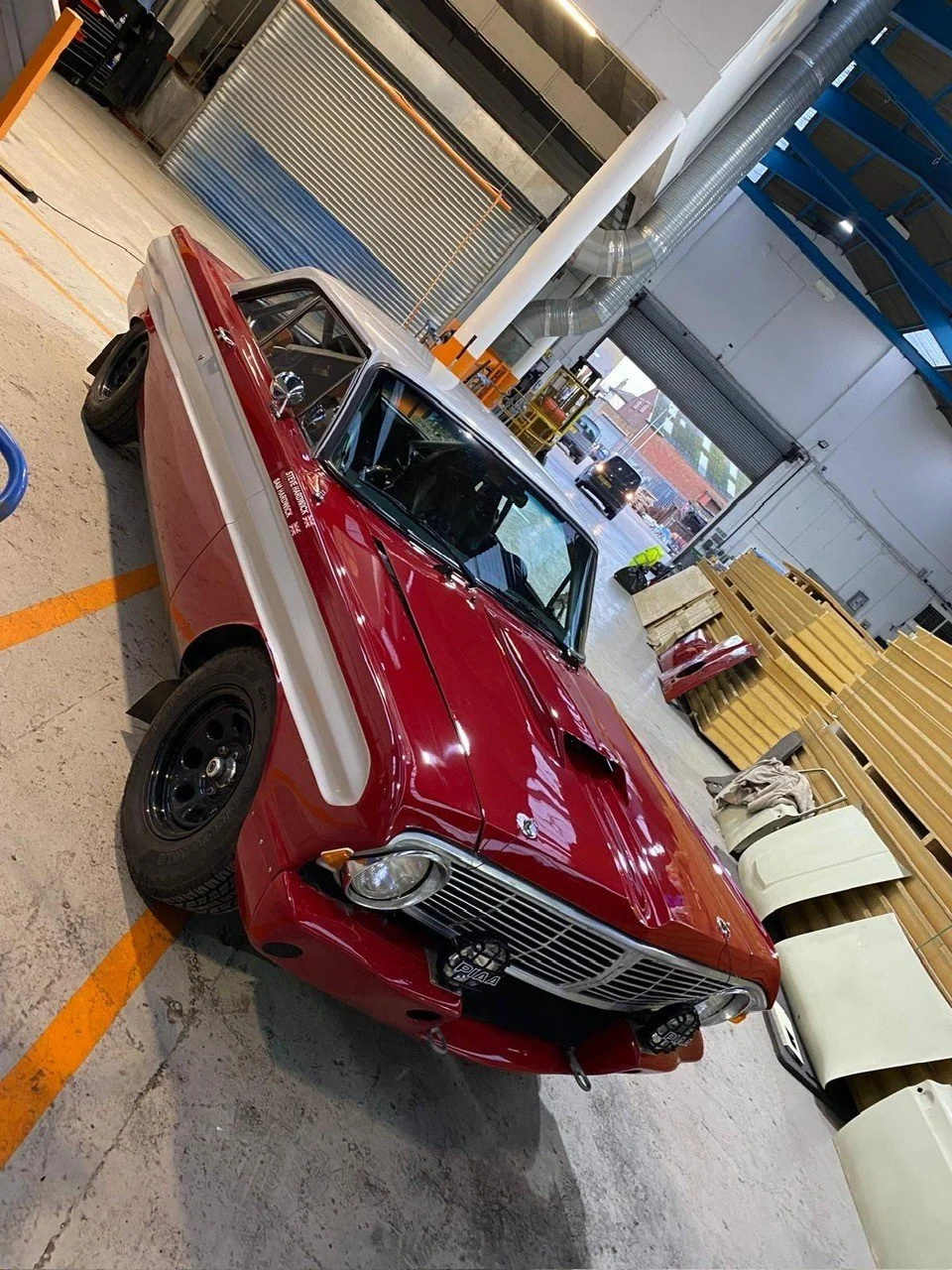 Red classic car with white stripe parked inside a workshop or garage.