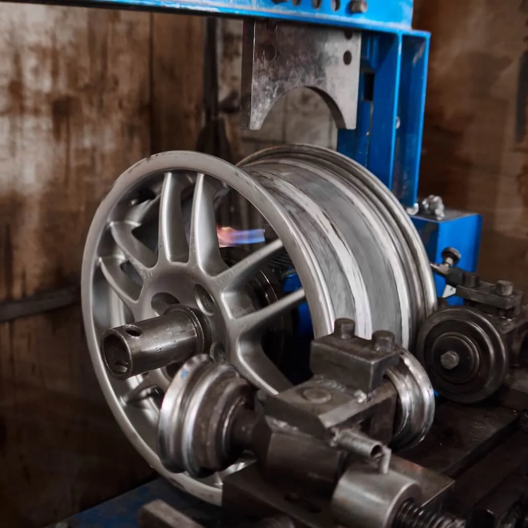 A wheel rim being heated with a torch on a blue metal machine in a workshop.
