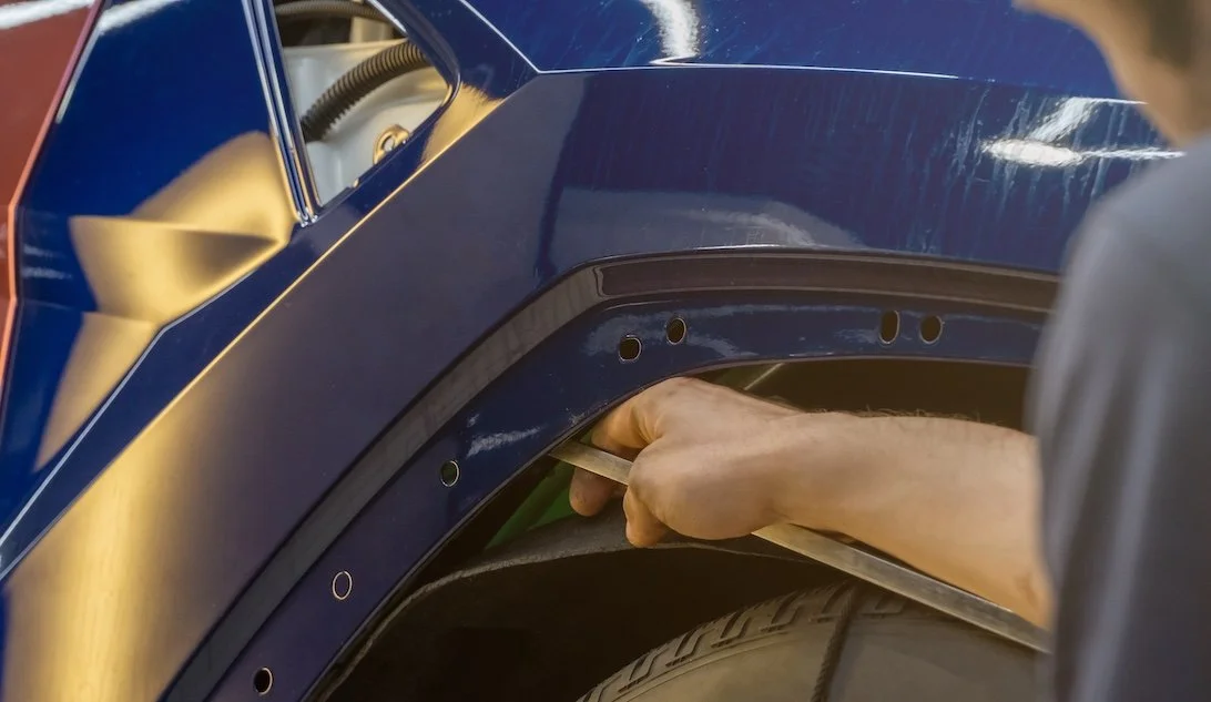 A person installing or repairing a part on a dark blue vehicle, possibly a fender or wheel arch, using a tool.