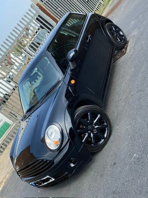 Black compact car parked on a street near a metal fence.