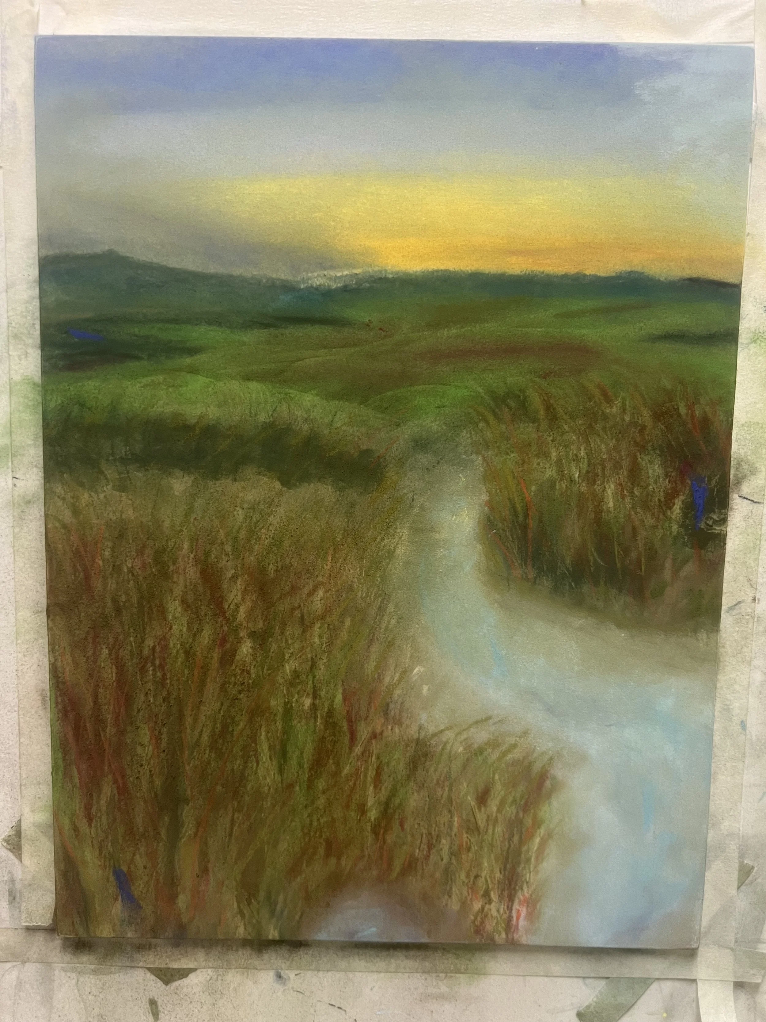 A landscape painting of a countryside at sunset, featuring green rolling hills, a winding dirt path, and a colorful sky with blue, yellow, and purple hues.