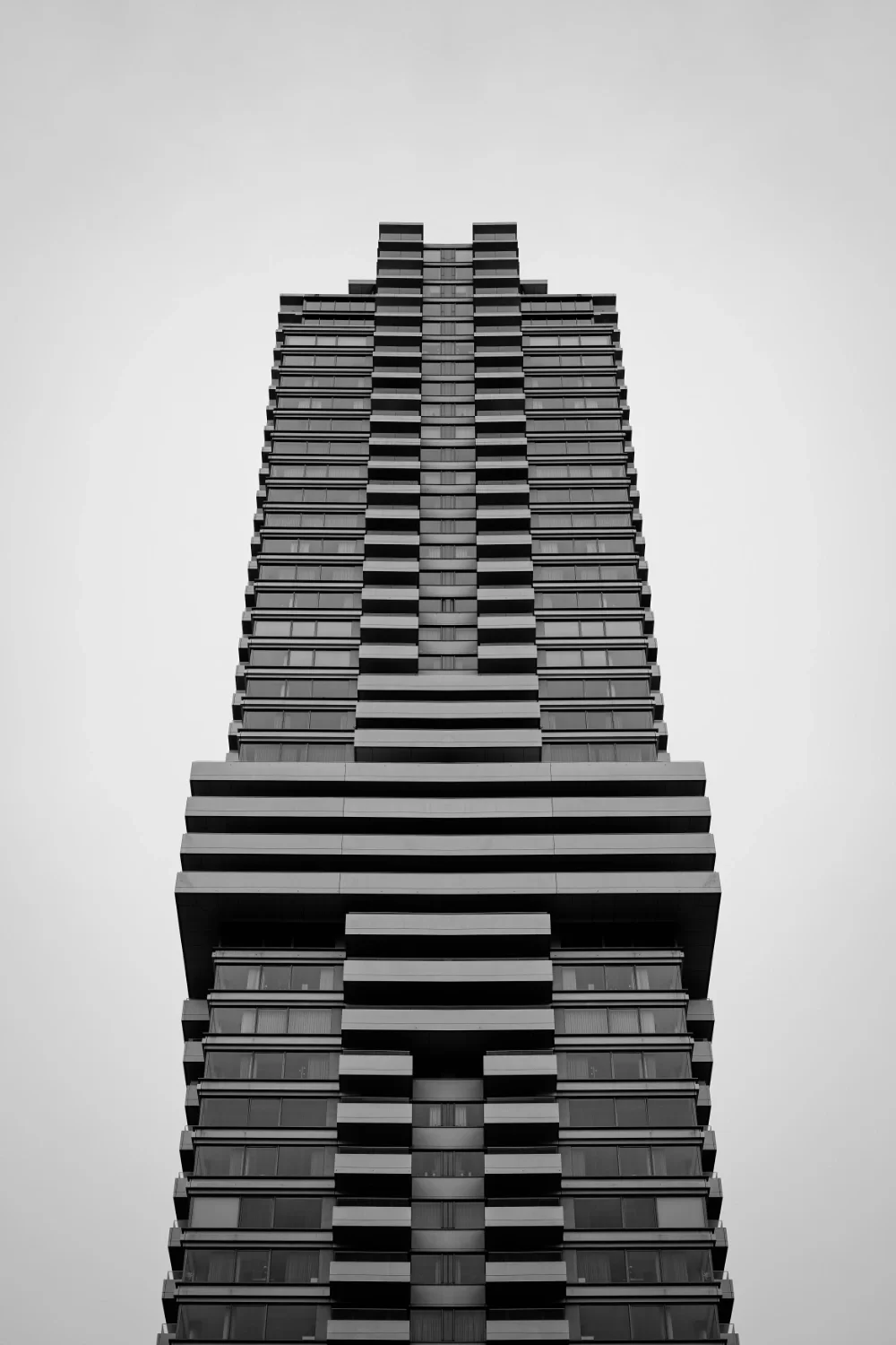 Low-angle black and white photo of a modern high-rise building against a cloudy sky.