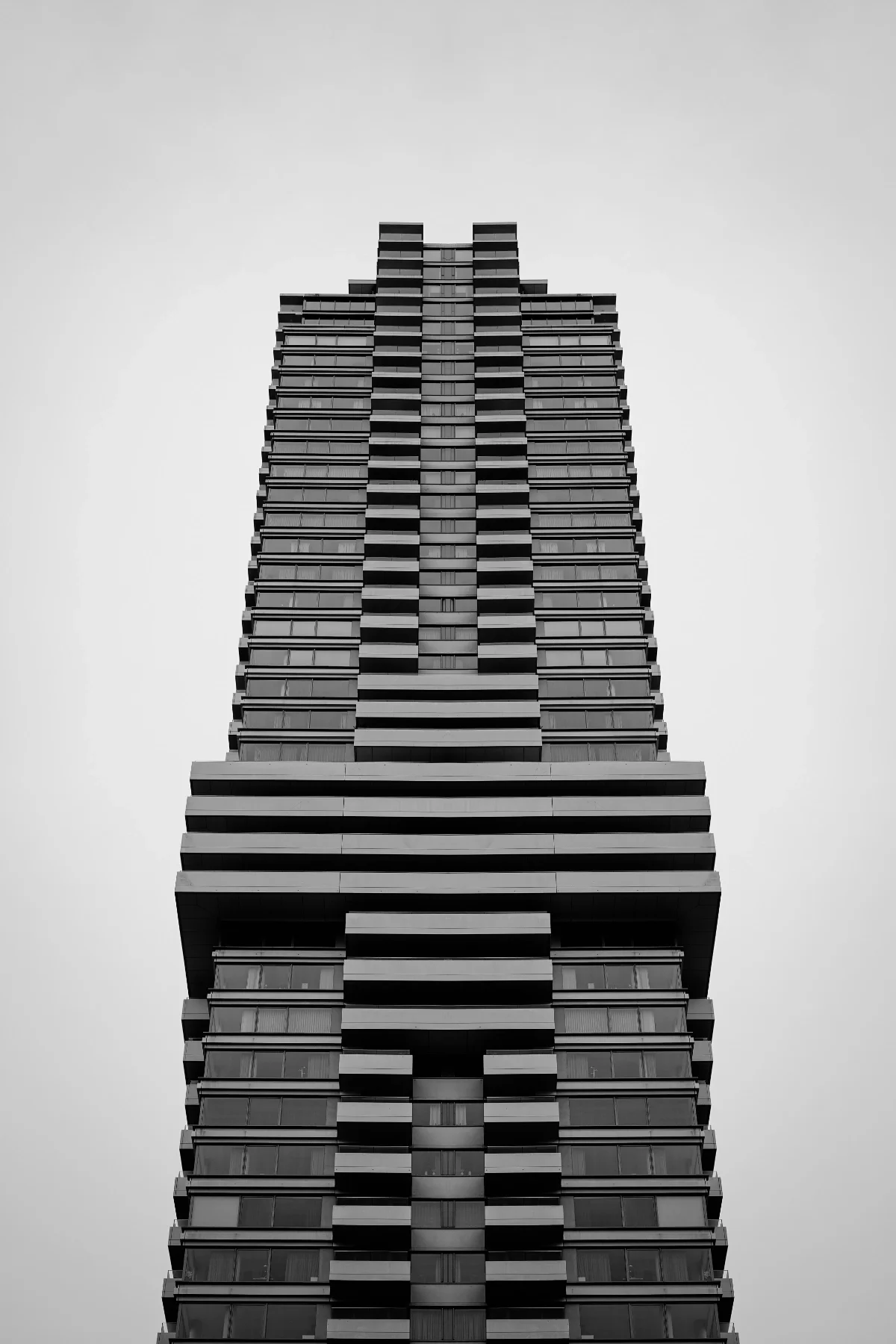 Low-angle view of a tall, modern apartment building with a symmetrical facade in black and white.