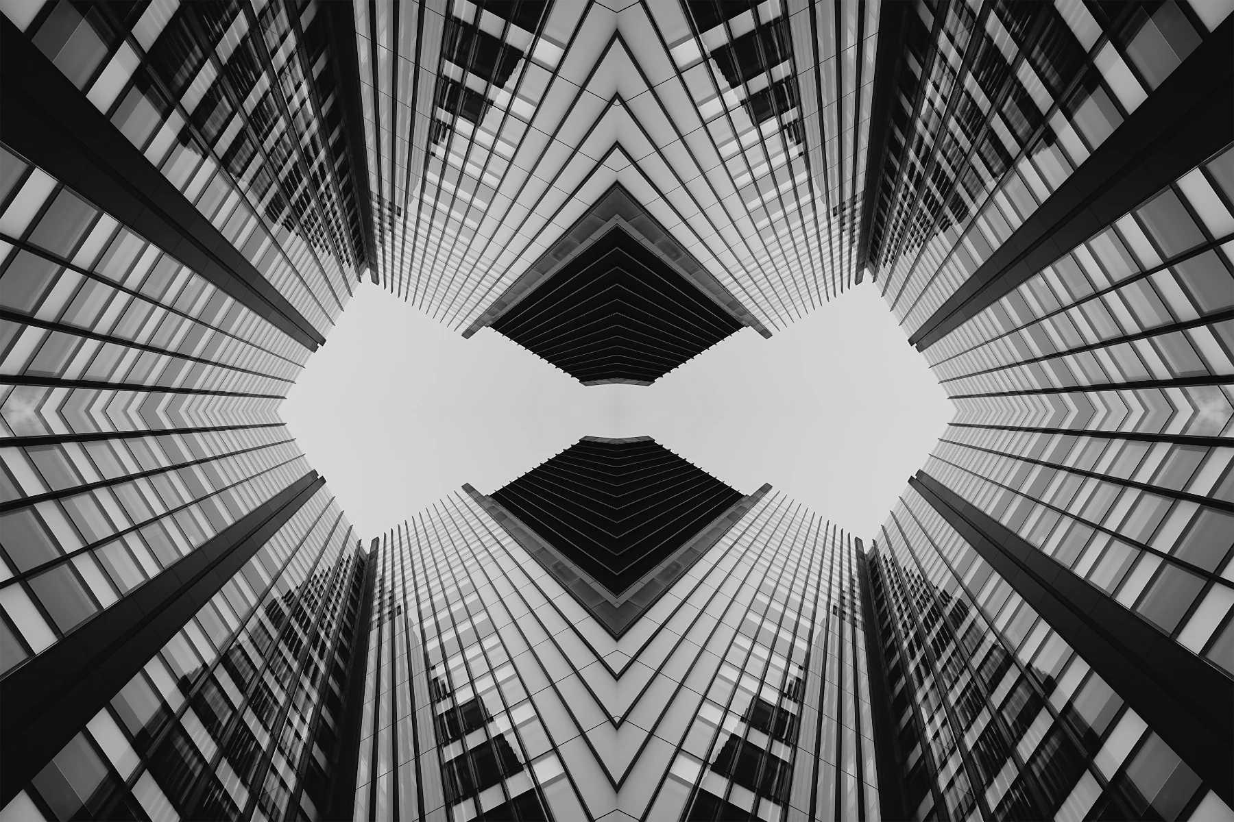 Looking up at tall modern glass skyscrapers from the ground, creating a symmetrical geometric pattern with a central open space in the sky.